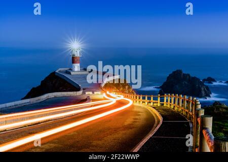 Bright trailing car lights lead to Cabo Ortegal lighthouse at night Stock Photo