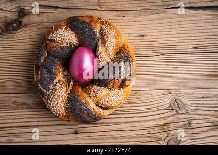Homemade Easter bread ring decorated with poppy sesame seeds, natural dyed purple egg on rustic wooden background, top view Stock Photo