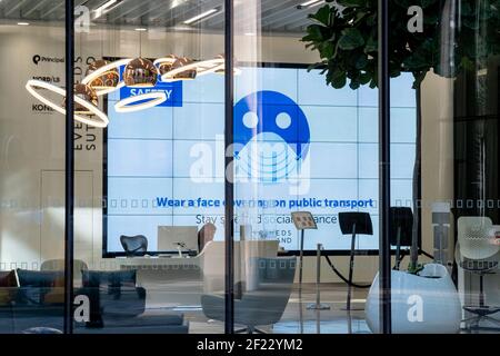 While office workers remain at home in accordance to government Covid guidelines and individual company policies, a solitary receptionist works alone beneath a screen with a message about hygiene and social distancing in the City of London, the capital's financial district, during the third lockdown of the Coronavirus pandemic, on 9th March 2021, in London, England. Stock Photo