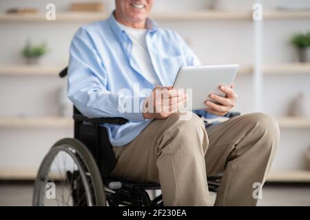 Cropped view of disabled senior man in wheelchair using tablet computer for online communication at home Stock Photo