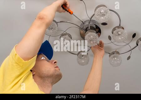 Electrician with glasses screws a chandelier to the ceiling in close-up Stock Photo