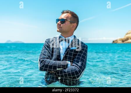 Happy man in a suit with a bow tie stands in the sea. Summer vacation concept. Stock Photo