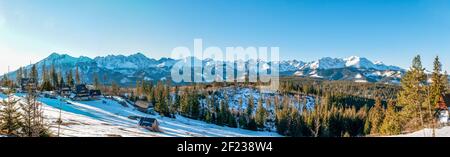 Wide winter panorama of Tatra Mountains in sunrise light with a village, houses and forest Stock Photo