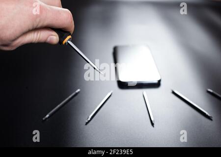Man's hand holding small screwdriver for fixinf phone and set od tools for reparing elecrtonics on black background. Stock Photo