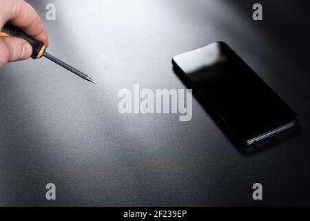 Hand with screwdriver for fixing electronics and smartphone on black background. Stock Photo