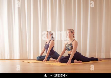 Two young women doing balance acro yoga in white studio Stock Photo - Alamy