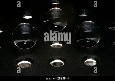 Three glass spheres in the hole on a metal grid support in black background Stock Photo