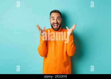 Image of excited and happy bearded man, shaking hands and smiling amazed, telling big news, standing over light blue background Stock Photo