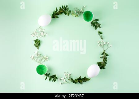 Easter frame made of eggs, flowers and green twigs on a green background, top view, flat lay, close up. Easter background. Stock Photo