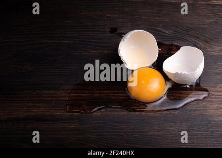 Broken chicken egg, yolk and egg white with shells on the dark wooden background, rustic style, close up Stock Photo