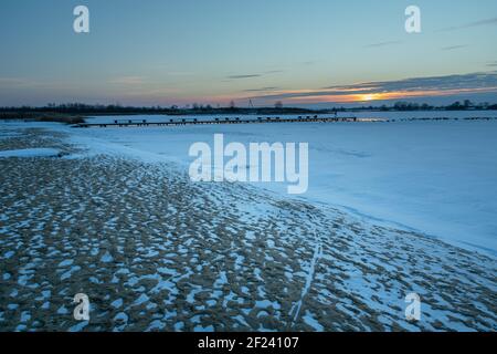 Sandy beach covered with snow and sunset over a frozen lake Stock Photo