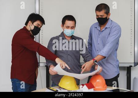 Confident team of architect and engineer wearing protective masks working together in a office. They discussing about new startup project on desk. Arc Stock Photo