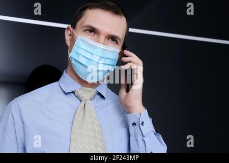 Portrait of man in protective face mask and office clothes talking on mobile phone, smartphone in male hand. Communication during coronavirus pandemic Stock Photo