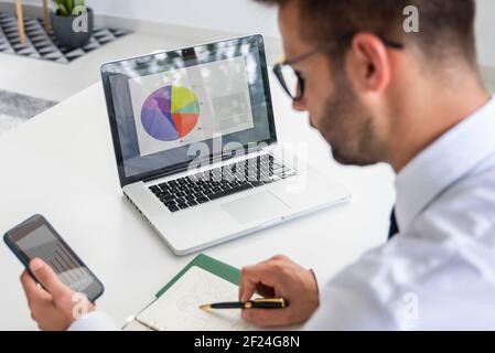 Rear view shot of financial advisor businessman analyzing financial graphs while working in the office. Stock Photo