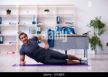 Young handsome employee doing sport exercises in the office Stock Photo