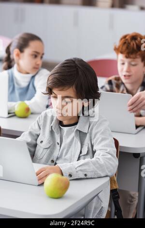 concentrated schoolboy near laptop and apple in classroom Stock Photo