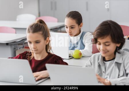 concentrated schoolchildren using laptops in school on blurred foreground Stock Photo