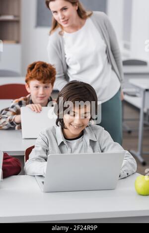 teacher standing near pupils using laptops during lesson, blurred background Stock Photo