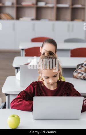 girl using laptop during lesson near classmates on blurred background Stock Photo