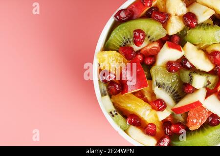 Bowl with fruit salad on a pink background. Juicy and ripe fruit slices. Top view Stock Photo