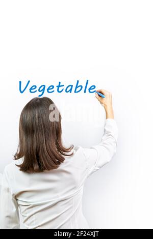 Woman writing the word Vegetables on a white background with a blue marker pen. Natural food concept Stock Photo