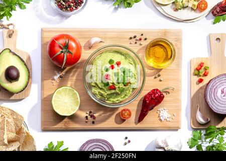 Flat lay composition. Guacamole with ingredients on wooden board on white background. Stock Photo