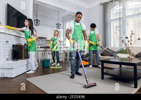 Team of diverse professional hardworking mixed race cleaners from cleaning service, working together in modern luxury house, using cleaning tools Stock Photo
