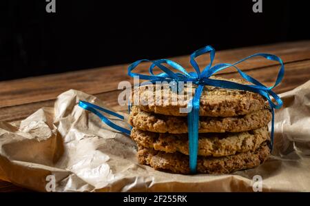 Homemade oatmeal cookies on parchment paper tied with a blue ribbon, gift wrapping, decoration. Wooden background. Space for text, side view. Stock Photo