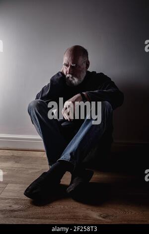 Elderly man sitting on the floor with his dog and looking at the camera ...