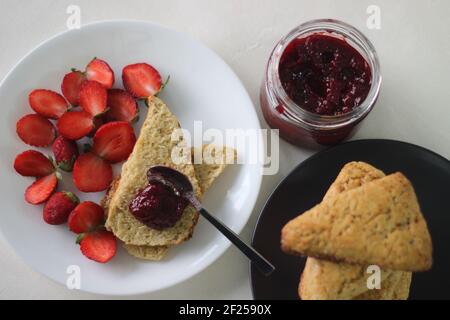 Home baked plain mildly sweet buttermilk scones served along with homemade strawberry jam and fresh cut strawberries. Shot on white background Stock Photo