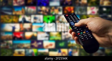 tv channels in background and remote control in hand. smart television and content on demand concept Stock Photo