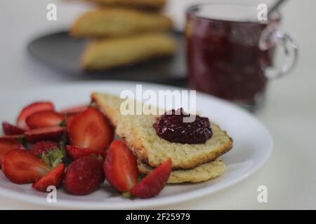 Home baked plain mildly sweet buttermilk scones served along with homemade strawberry jam and fresh cut strawberries. Shot on white background Stock Photo