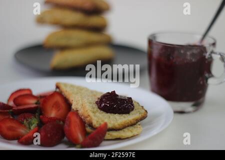 Home baked plain mildly sweet buttermilk scones served along with homemade strawberry jam and fresh cut strawberries. Shot on white background Stock Photo