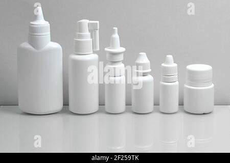 Monochrome grey color photo. A set of medical plastic white bottles, demonstrating a variety of medicinal forms, on a gray background. Stock Photo