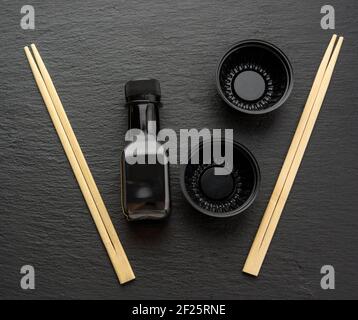 Wooden sticks for sushi, bottle of soy sauce and disposable plastic plates on black background Stock Photo