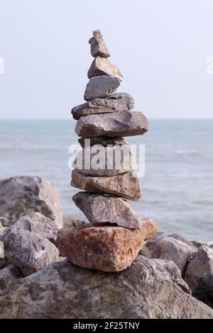 Cairn of balanced stones or stacked rocks balancing on beach or shoreline with sea behind Stock Photo