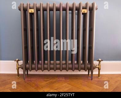 Old fashioned cast iron radiator with brass fittings on herringbone wooden floor Stock Photo