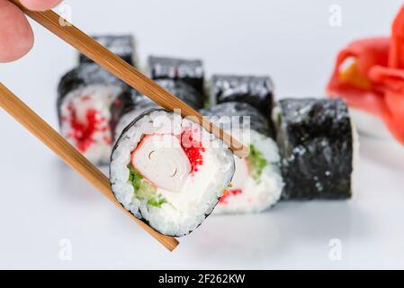 close up of chopsticks taking portion of sushi roll on the table restaurant / eating sushi roll using chopsticks Stock Photo