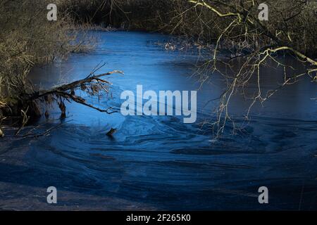 A beautiful picture of a small pond covered with ice. Blue icy water with trees in the background Stock Photo