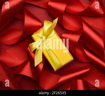 Gift box is packed in yellow paper and curled red silk ribbon on a red background, Stock Photo