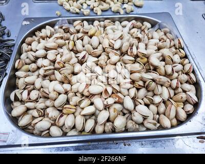 A shot of lots of pistachio cashew seeds in shells in a metal square tray with rounded corners surrounded by other nuts and seeds. Stock Photo