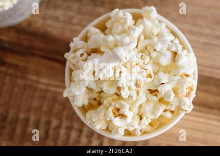 A bucket of popcorn, top-view, warm colors, light brown wooden background, flat lay, daylight macro close-up Stock Photo