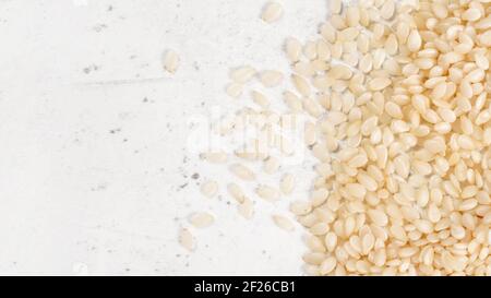 White sesame - Sesamum indicum - seeds on white stone like board, view from above, space for text left side Stock Photo