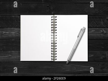 Blank open spiral notebook and pen isolated on black wood background Stock Photo