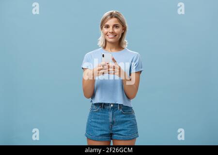 New phone is fantastic. Portrait of satisfied happy young modern blond woman in trendy outfit with blond short haircut smiling j Stock Photo