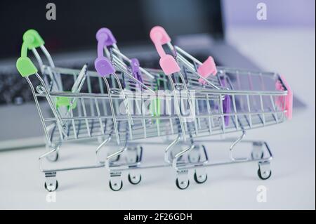 three miniature shopping carts in front of a laptop Stock Photo