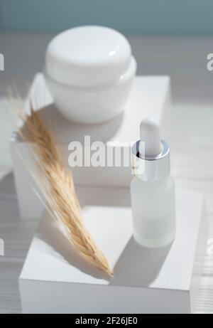 Cosmetic products cream and pipet bottle on white boxes and wheat stalk Stock Photo