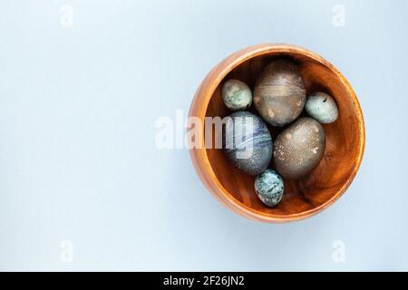 Creatively painted chicken and quail Easter eggs with natural hibiscus dye, look like sea stones in bowl on gray background, copy space. Happy Easter Stock Photo