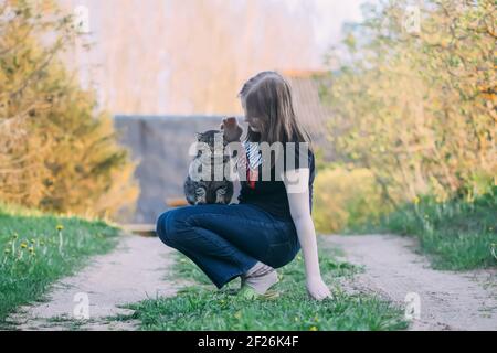 The teenager girl playing with her lovely striped grey cat outdoors on spring nature background in countryside Stock Photo