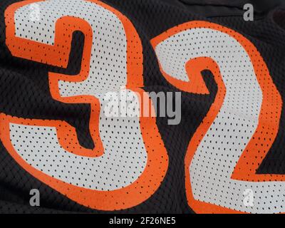 Orange and white numbers display 32 up close on a black mesh sports jersey. Stock Photo